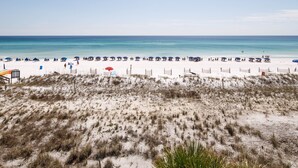 A beach with white sand, blue umbrellas, and a wooden fence. - PI 307: Sunkissed & Vibing. Absolutely beautiful, Gulf front, WiFi (Fort Walton Beach)