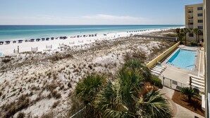 A beach view from a hotel balcony with a pool and beach umbrellas. - PI 307: Sunkissed & Vibing. Absolutely beautiful, Gulf front, WiFi (Fort Walton Beach)