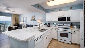 A modern kitchen with white cabinets, a large island with a sink, and a view of the ocean through a balcony. - PI 307: Sunkissed & Vibing. Absolutely beautiful, Gulf front, WiFi (Fort Walton Beach)