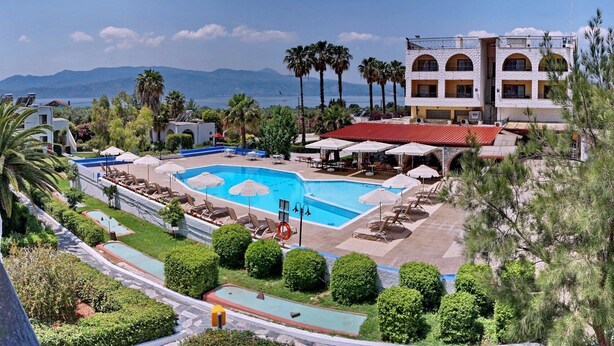 A hotel with a large swimming pool, outdoor seating, and a view of the mountains. - Silver Bay Hotel & Bungalows (Lesvos)