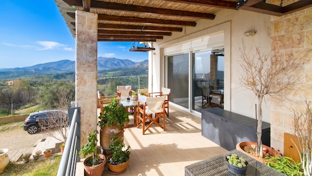 A balcony with a view of mountains, a table with chairs, and potted plants. - The House Olympia (Archaia Olympia)