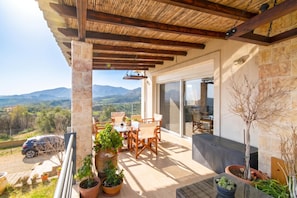 A balcony with a view of mountains, a table with chairs, and potted plants.