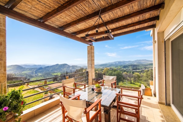 A covered outdoor seating area with a table and chairs, overlooking a scenic landscape.