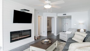 Una sala de estar moderna con chimenea, un televisor de pantalla plana montado encima y un ventilador de techo, además de un sofá con almohadones.