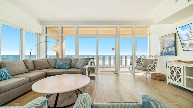 A spacious living area with a large window overlooking the beach, a round wooden table, and comfortable seating. - 4BR, Beachfront, 3RD FLOOR - Parking level!, Waterslide! (Gulf Shores)