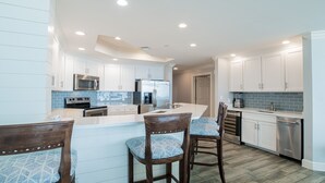 A modern kitchen with white cabinets, stainless steel appliances, and a bar area with wooden chairs.