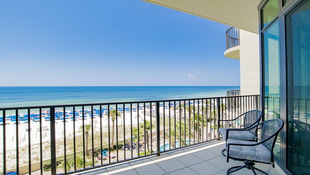 A balcony with a view of a beach, a pool, and a chair.