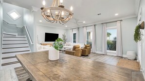 Un salon spacieux avec une table à manger en bois, un lustre, un canapé blanc et un téléviseur fixé au mur.