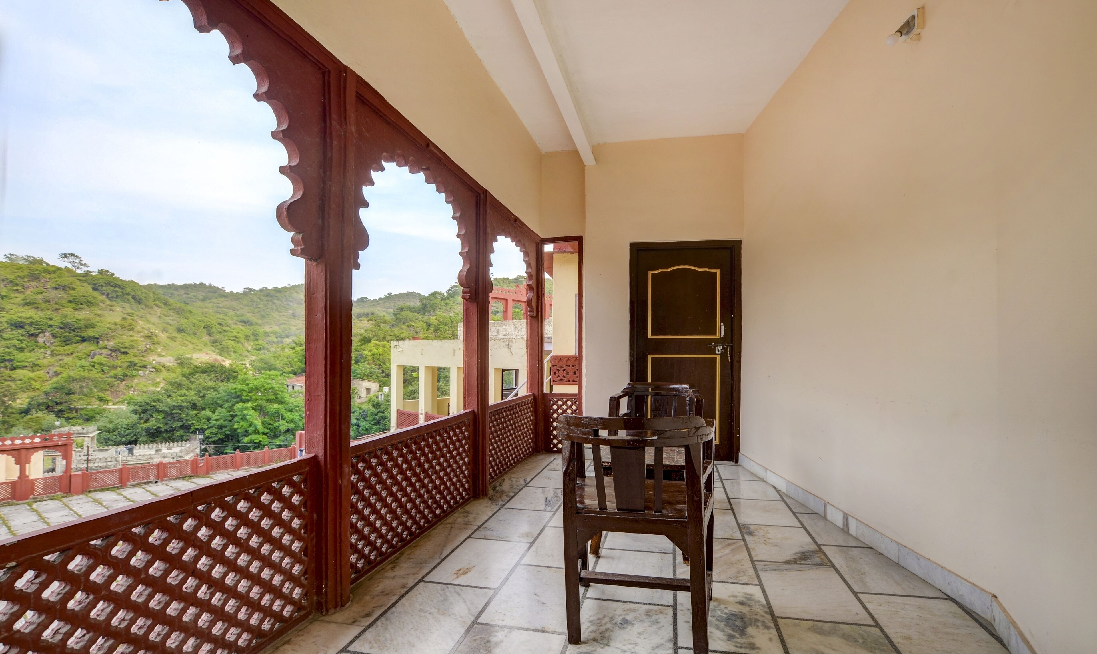 A balcony with a wooden chair and a table, a door, and a view of a green hillside.
