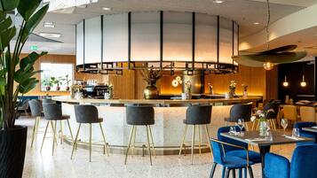 Uma área de bar moderna com uma ilha central, banquetas e cadeiras azuis.