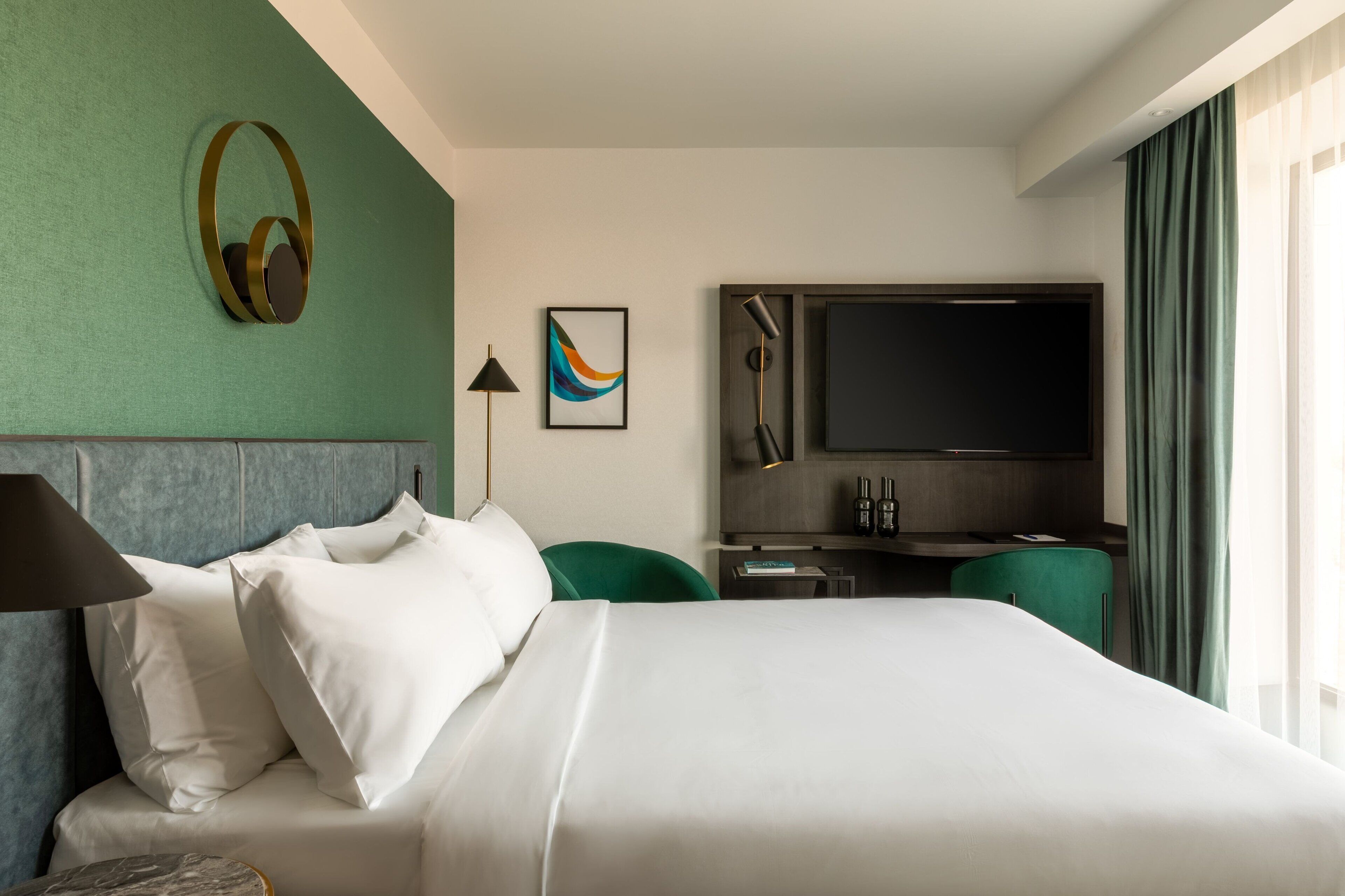 Ein Hotelzimmer mit Bett, Schreibtisch, Fernseher, Lampe und einer grünen Wand.