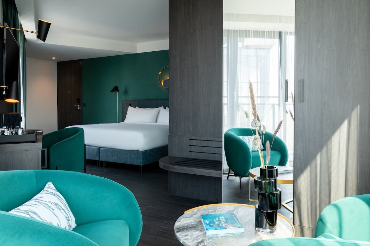 A modern hotel room with a bed, a desk, a chair, and a round table.