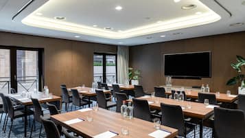 Una sala de conferencias con varias mesas, sillas, un televisor plano grande y una planta en maceta.