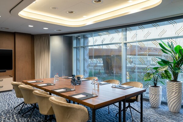 A conference room with a long table, chairs, a television, and large windows with a view of the outside.