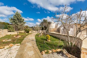 Un sendero de piedra serpentea por un jardín ajardinado con diversas plantas y un árbol grande.