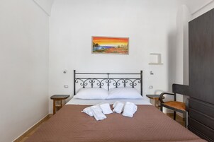 Una cama bien tendida con sábanas blancas, un edredón marrón y un cuadro de un atardecer en la pared.