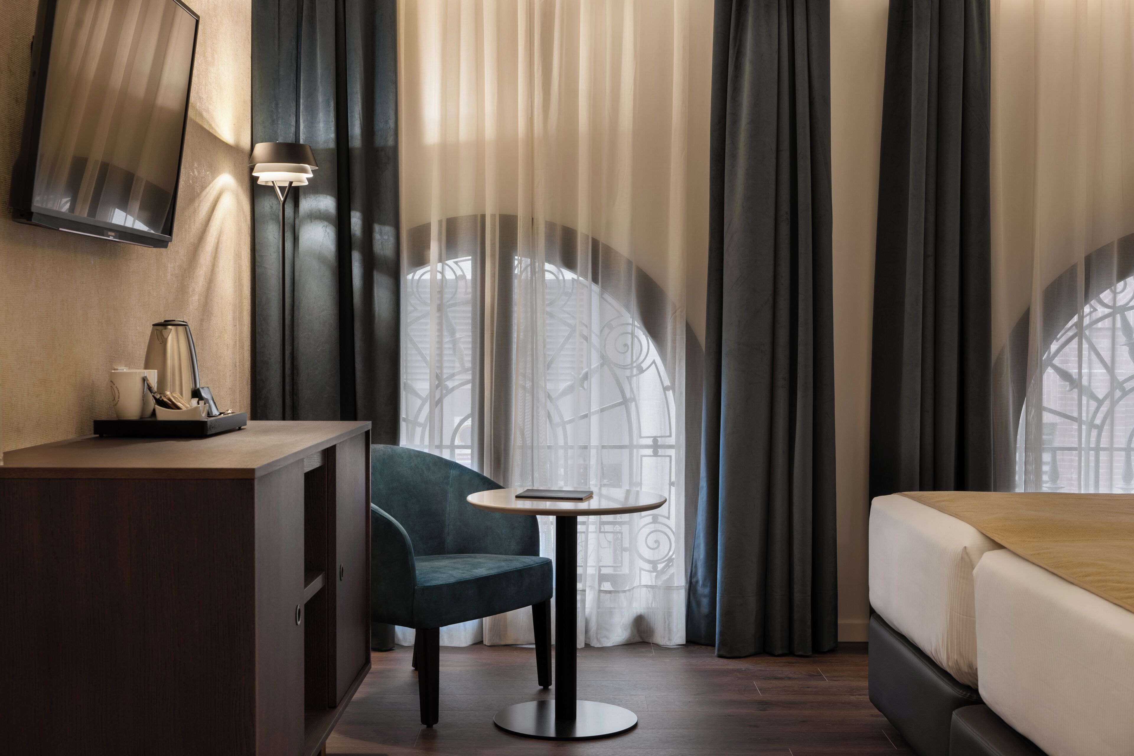 Camera d'albergo con un letto, una scrivania con una lampada, una sedia e un tavolino.