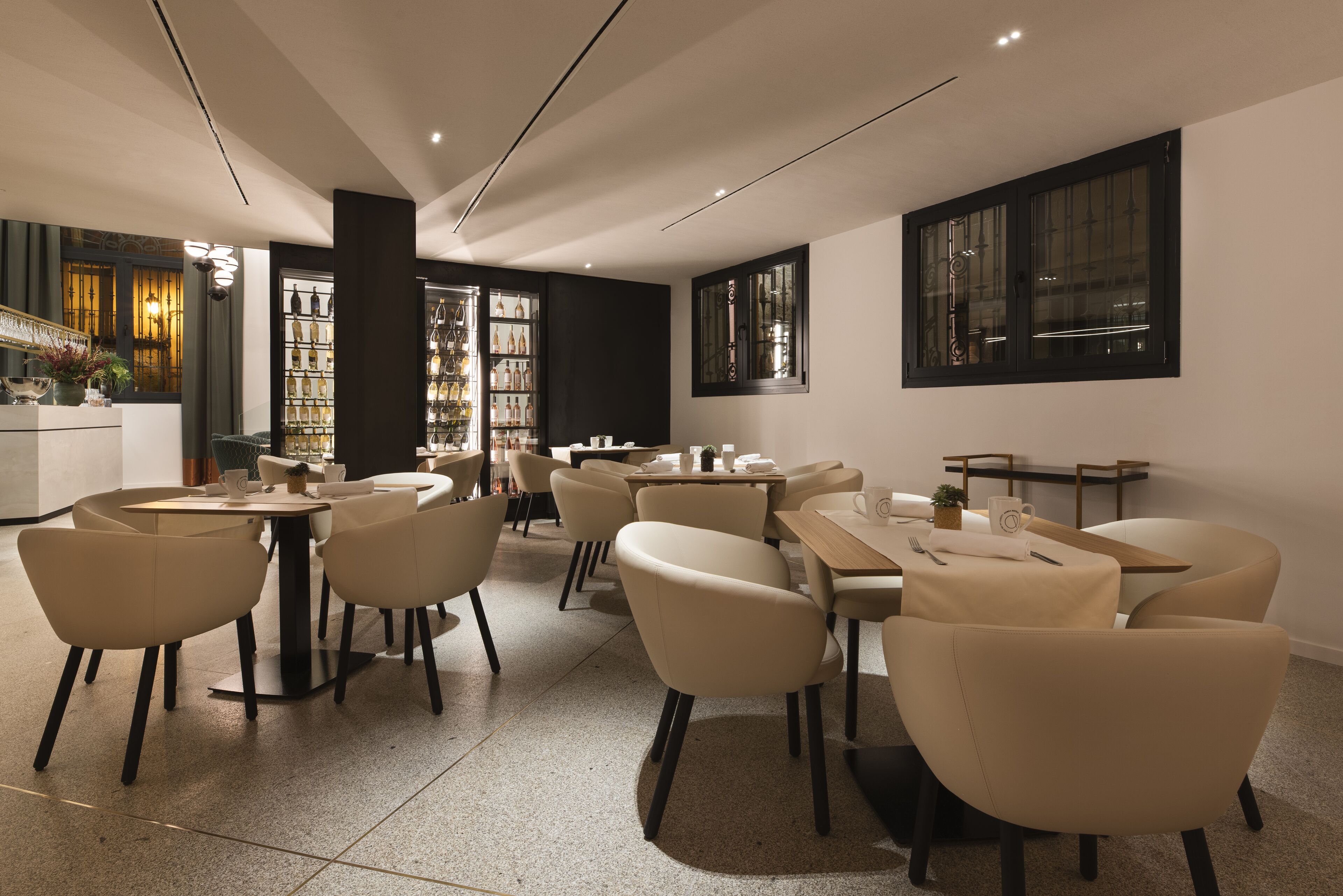 A modern restaurant interior with round tables and chairs, a bar area, and a view of the city through large windows.