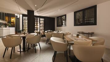 A modern restaurant interior with round tables and chairs, a bar area, and a view of the city through large windows.