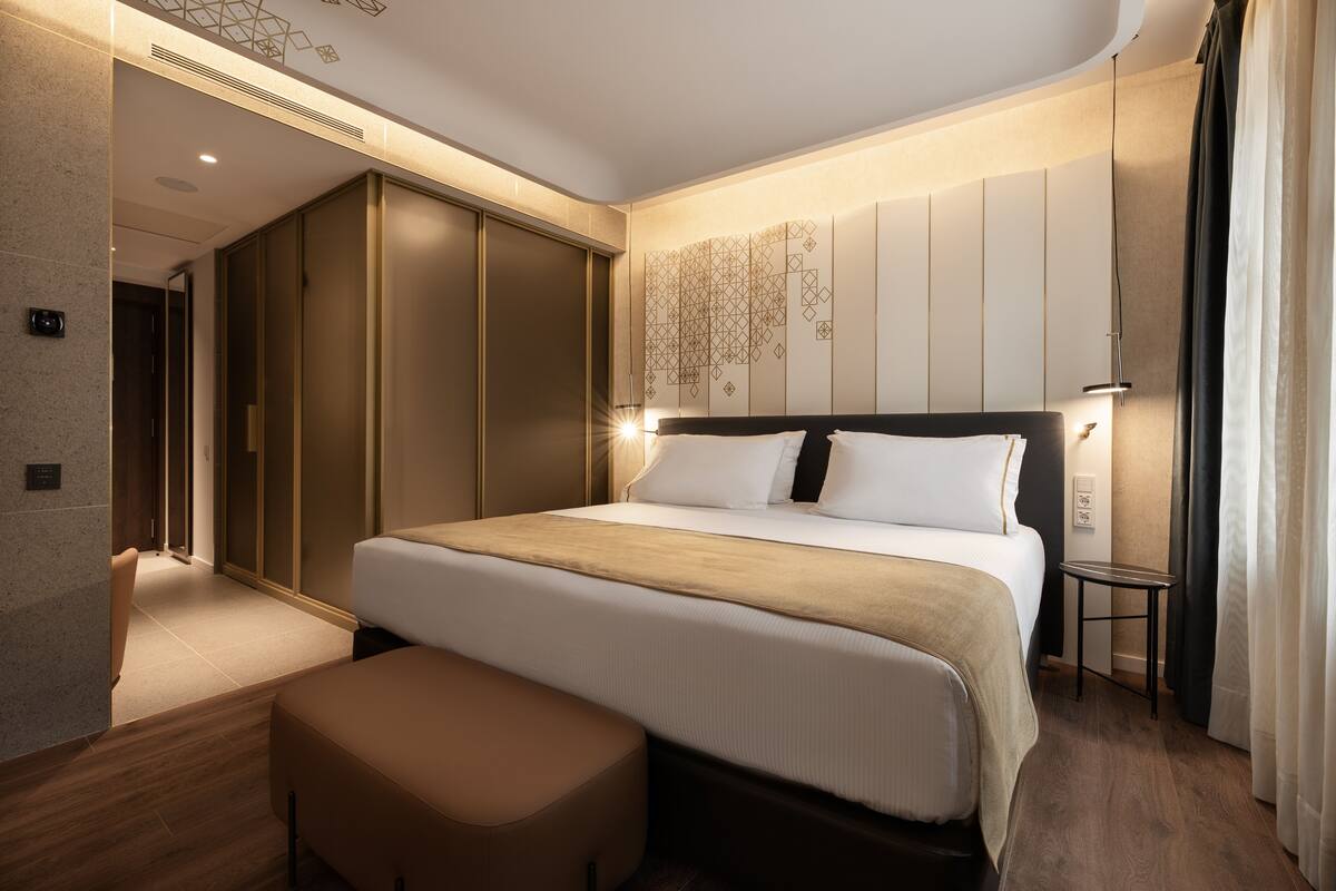 Ein modernes Hotelzimmer mit einem großen Bett, einem Nachttisch, einer Bank und einem Kleiderschrank.
