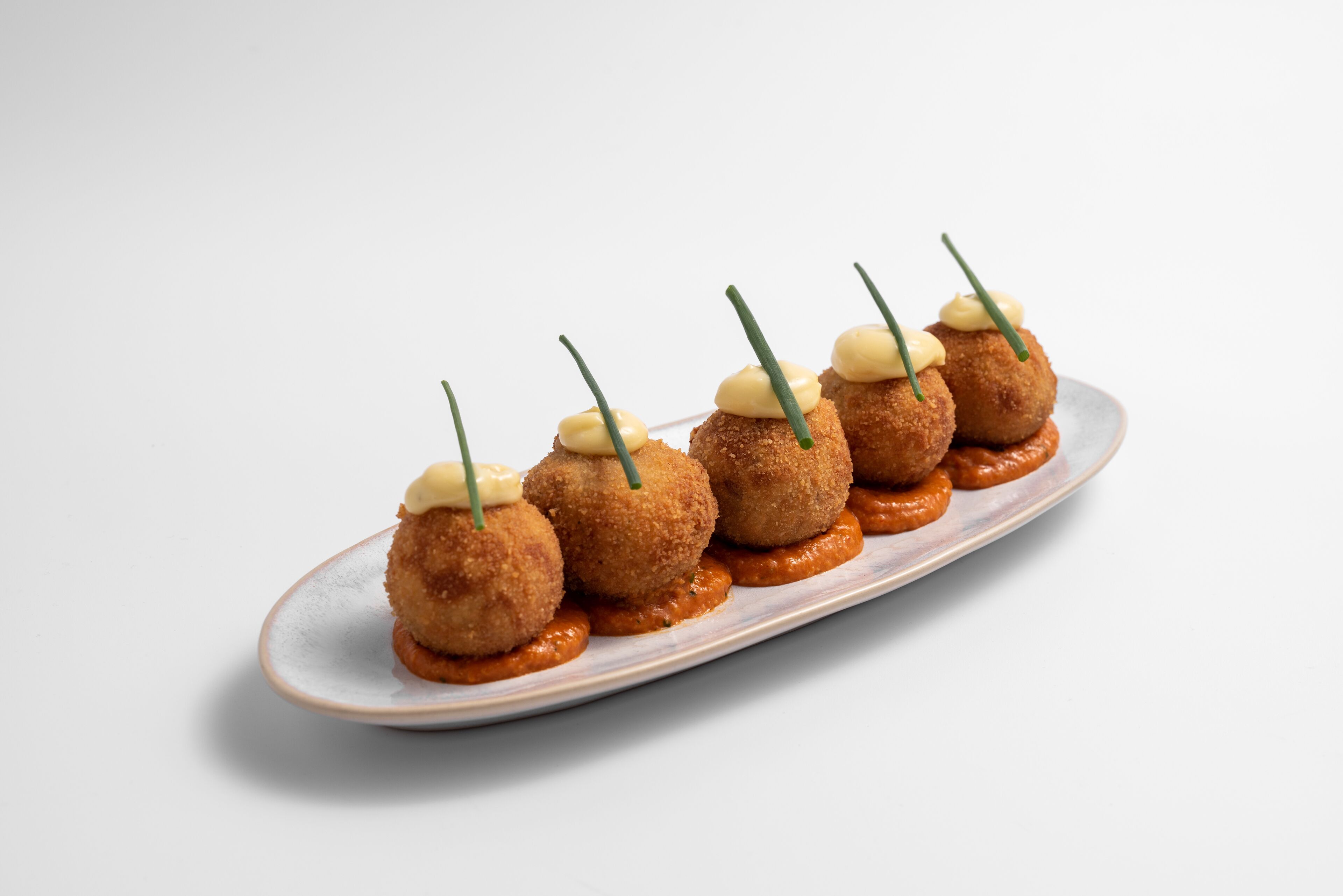 A plate of breaded and fried balls with a creamy sauce and garnish.
