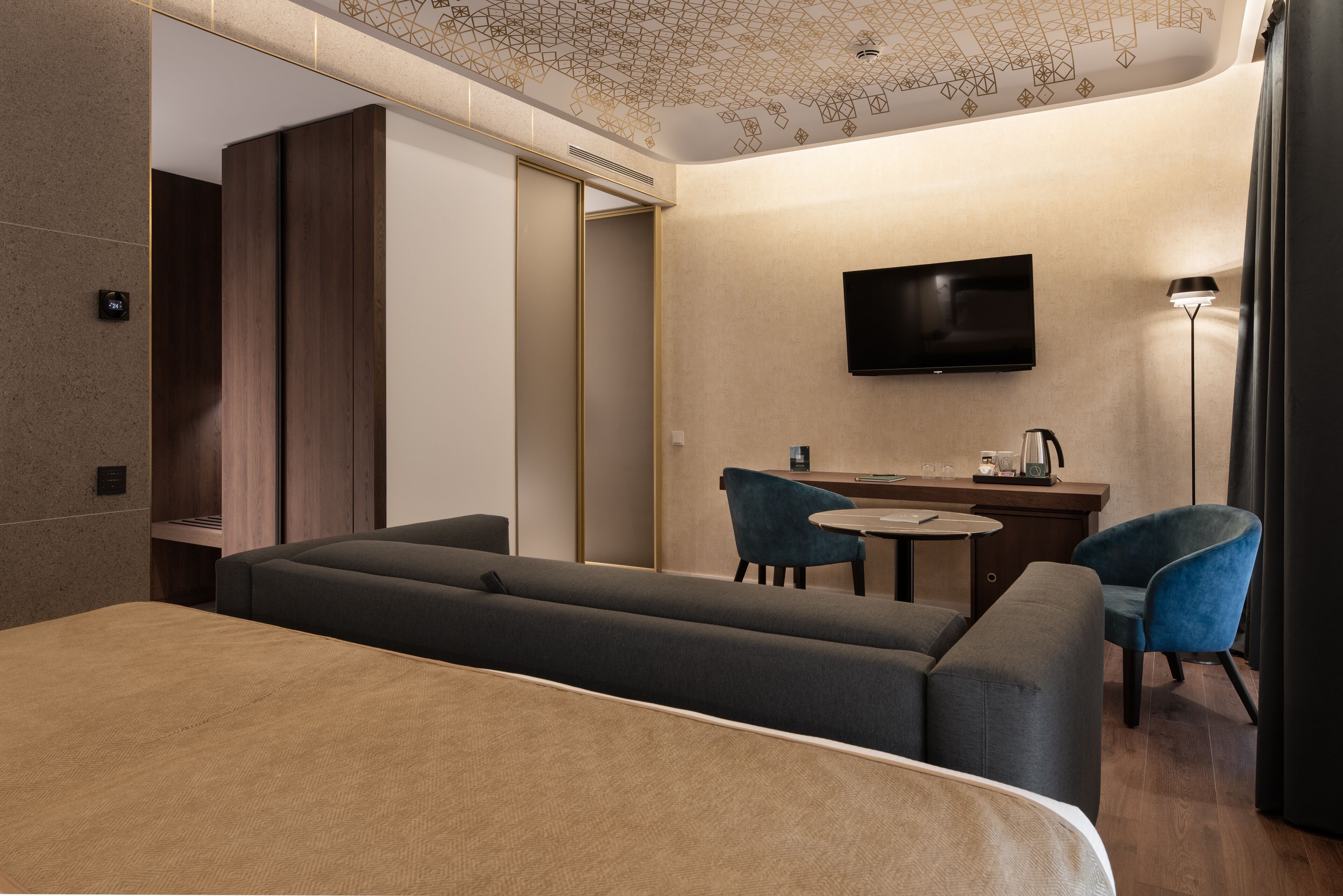 Una habitación de hotel moderna con una cama grande, un escritorio con silla, un televisor y una cafetera.