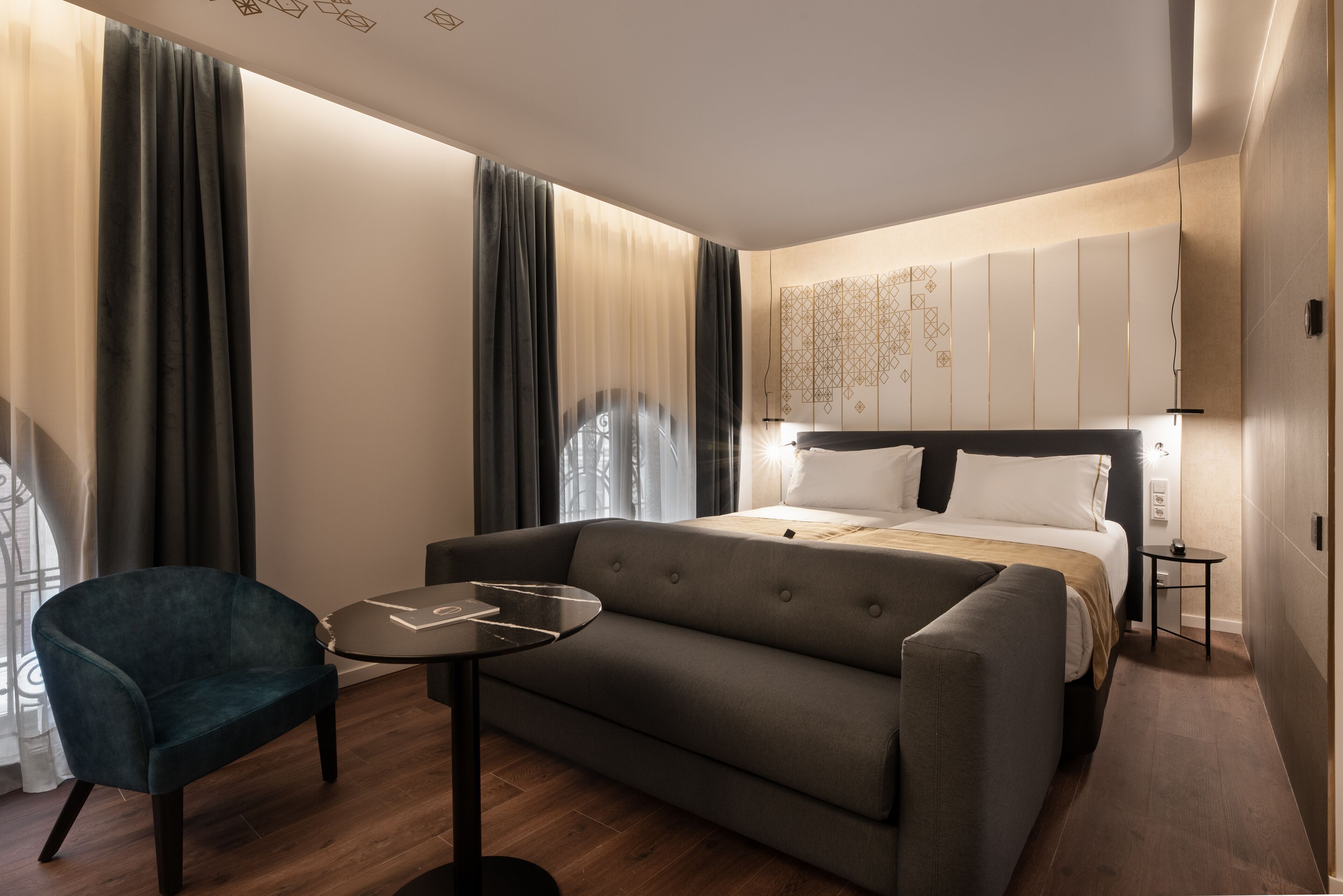 A modern hotel room with a bed, a sofa, a small table, and a chair.