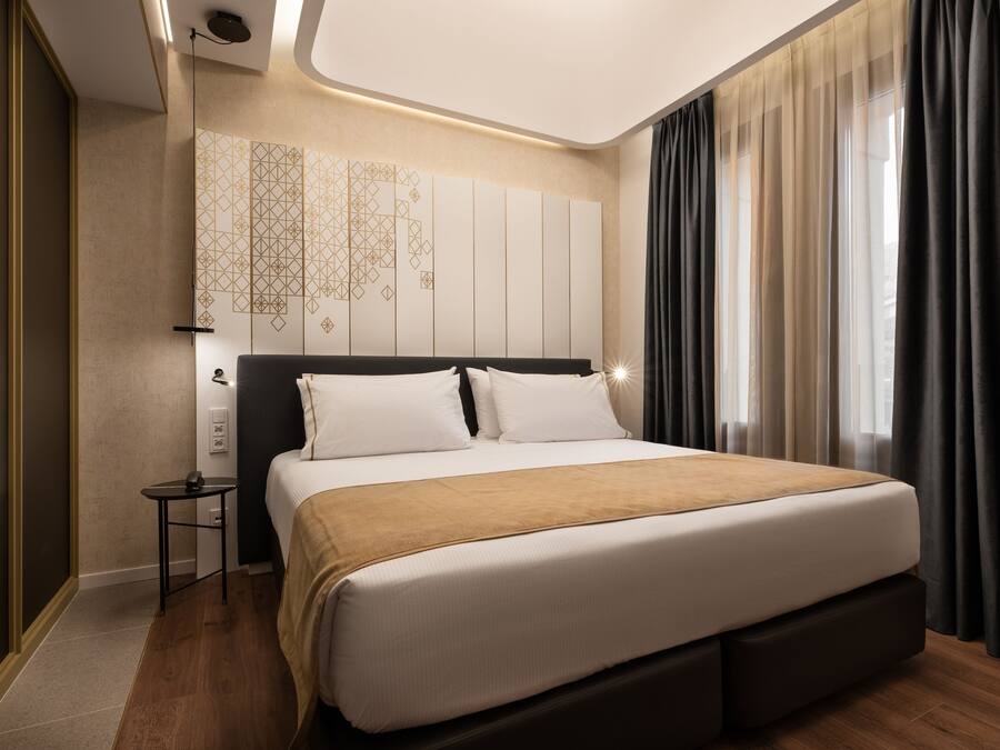 Habitació d'hotel moderna amb un llit gran, una taula de nit, televisió penjada a la paret i una finestra amb cortines.