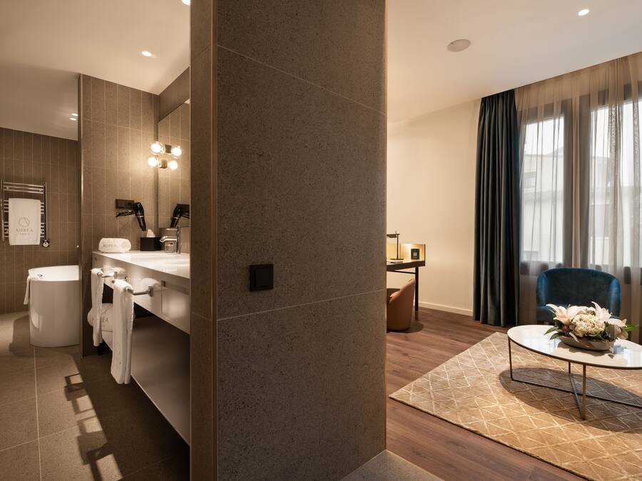 Une salle de bain moderne avec une baignoire, un lavabo et un miroir. On y trouve un porte-serviettes avec des serviettes, des toilettes et un espace douche. La salle de bain est dotée d’un grand miroir avec des lumières au-dessus.