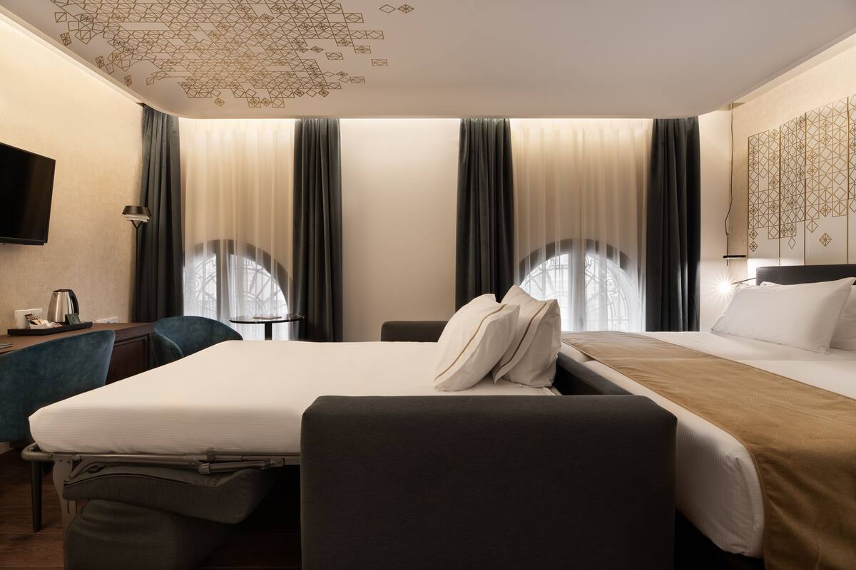 Ein Hotelzimmer mit einem Bett, einem Schreibtisch, einem Stuhl, einem Fernseher und einem fenster mit Vorhängen.
