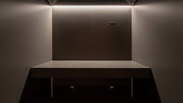 A minimalist room with a central light source, a flat surface, and a small control panel.