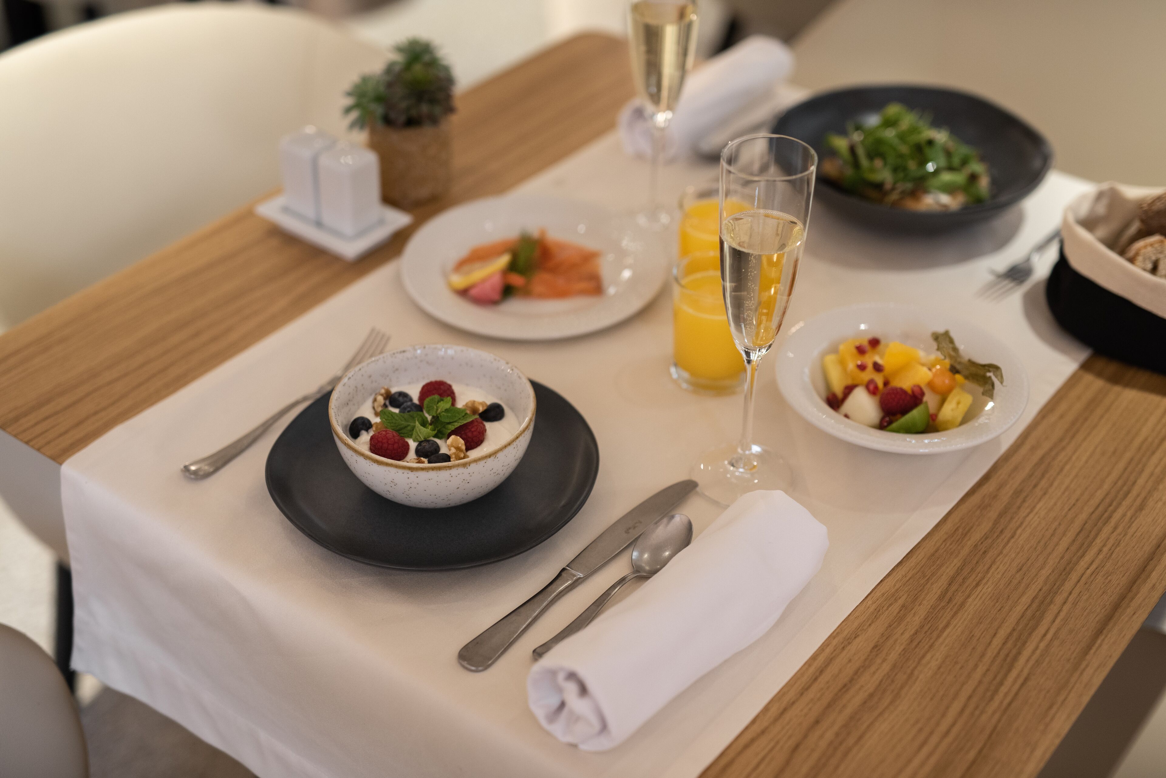 Een ontbijtsetting met een kom yoghurt belegd met bessen, een glas sinaasappelsap en een schaal fruitsalade.