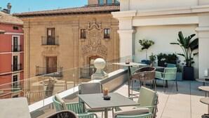 Eine Dachterrasse mit Sitzgelegenheiten im Freien, einer Zierwand und Blick auf angrenzende Gebäude.