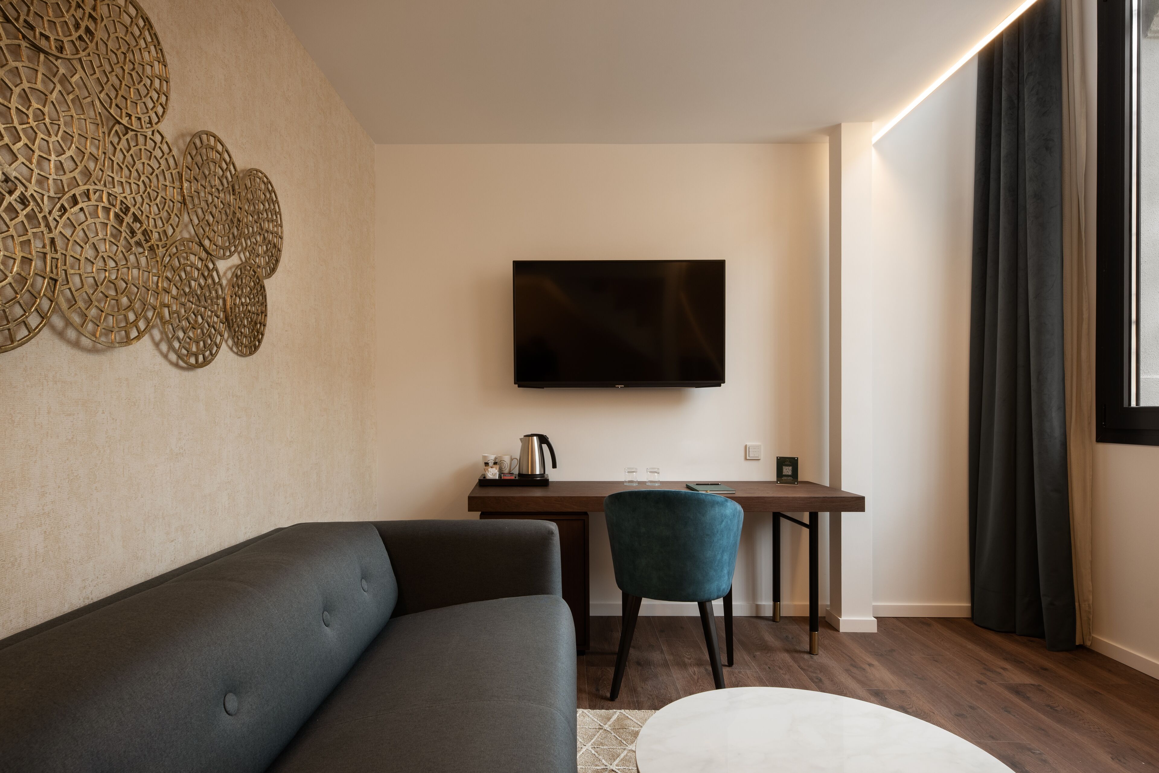 Una sala de estar moderna con un sofá, un escritorio, una silla y un televisor de pantalla plana montado en la pared.