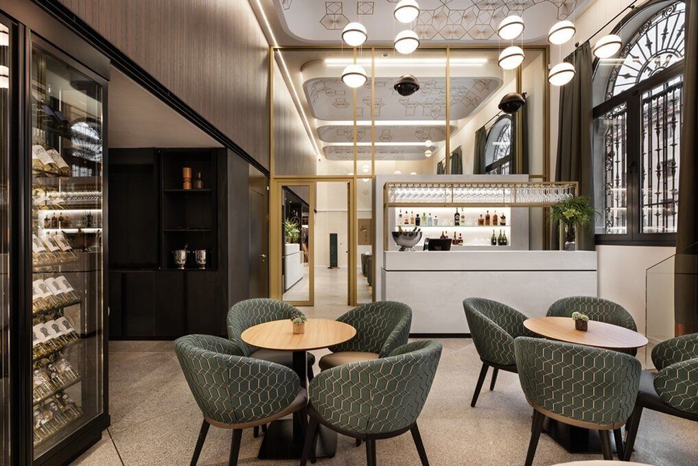 Un interior moderno con una zona de bar, asientos con sillas estampadas y una vitrina de vidrio.