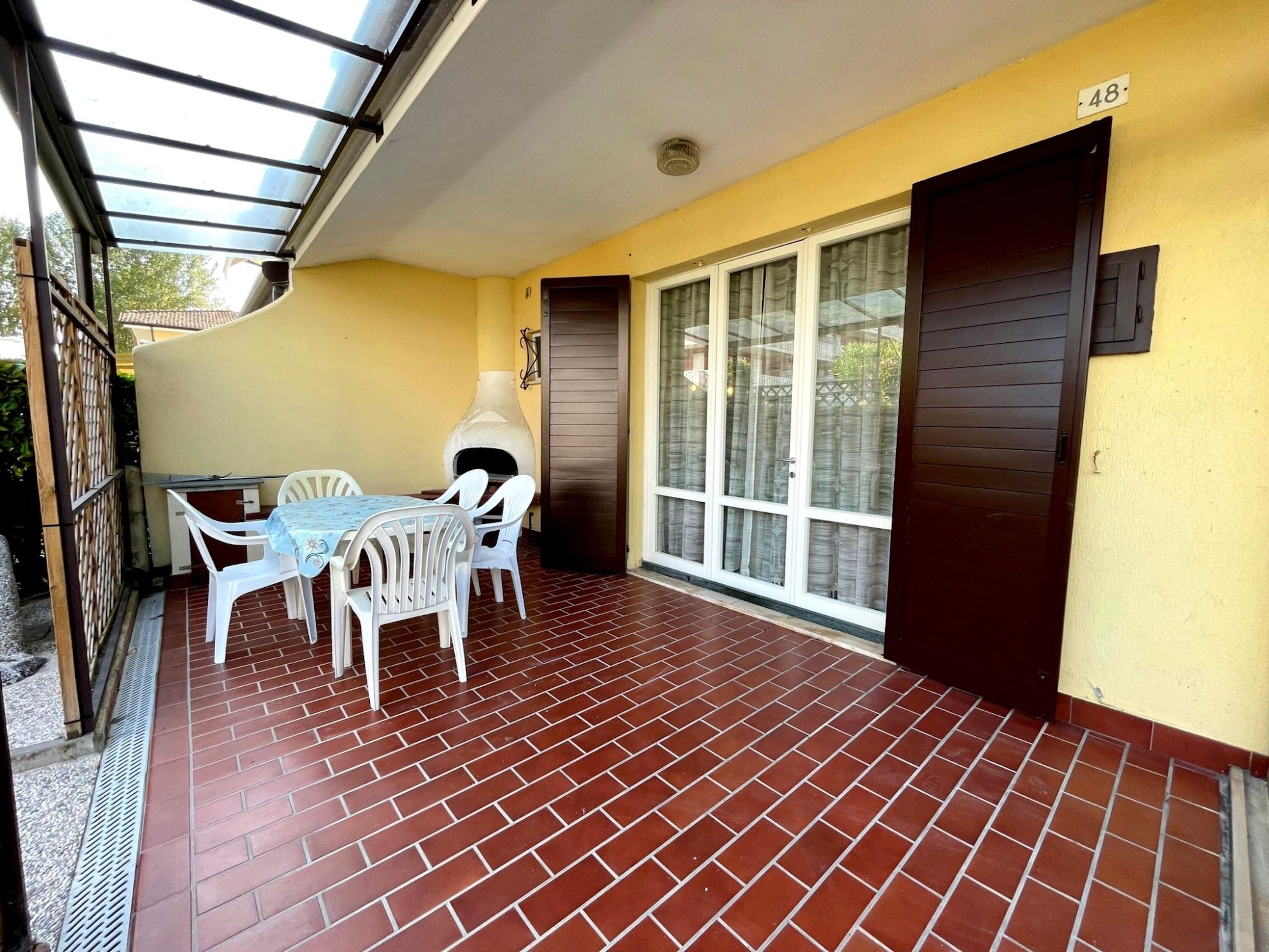 Un patio techado con suelo de ladrillo, una mesa con sillas y un amplio ventanal corredera.