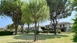 Una zona residenziale con un prato curato, diversi alberi maturi e una casa a due piani con un balcone.