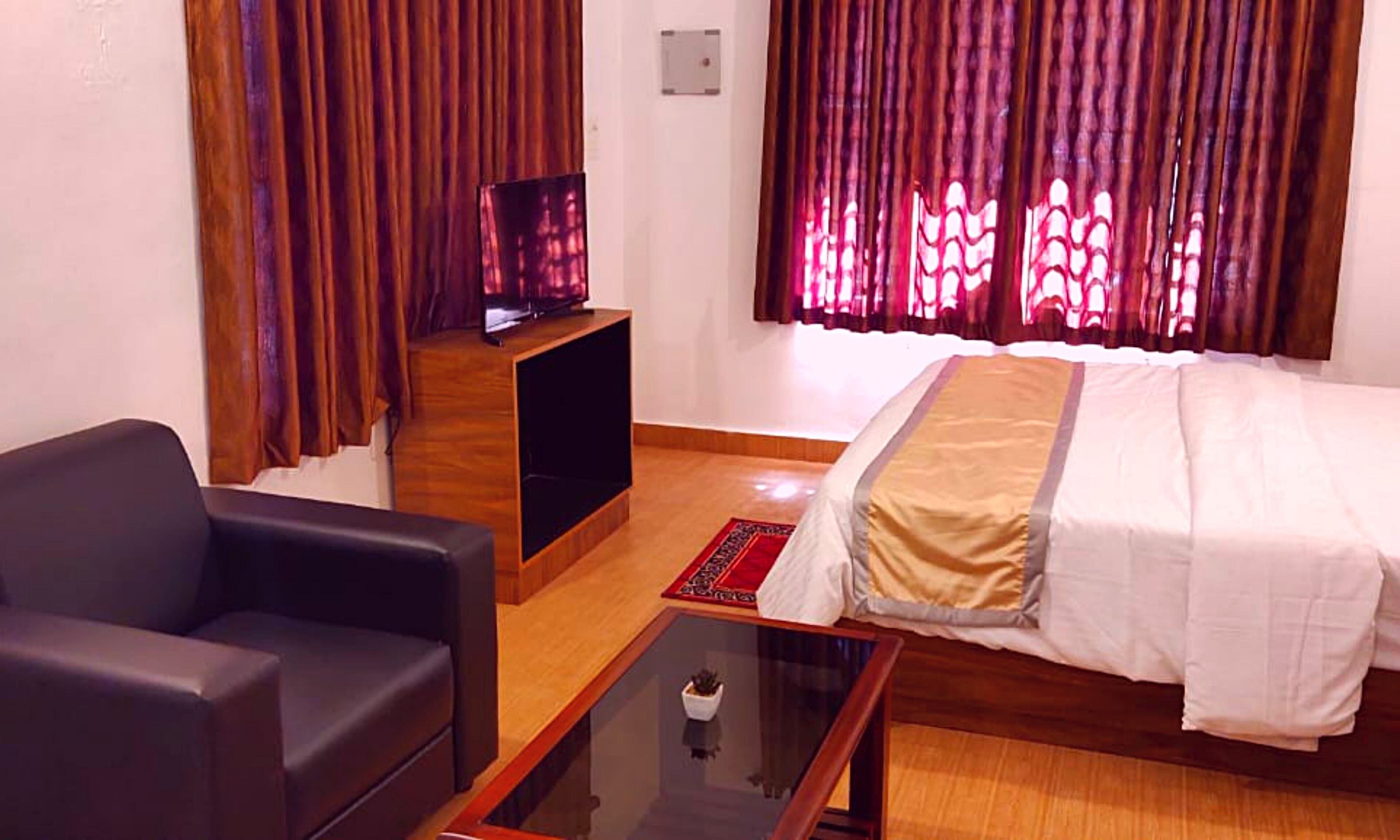 Habitación de hotel con cama, sofá, televisor sobre un mueble de madera y ventana con cortinas.