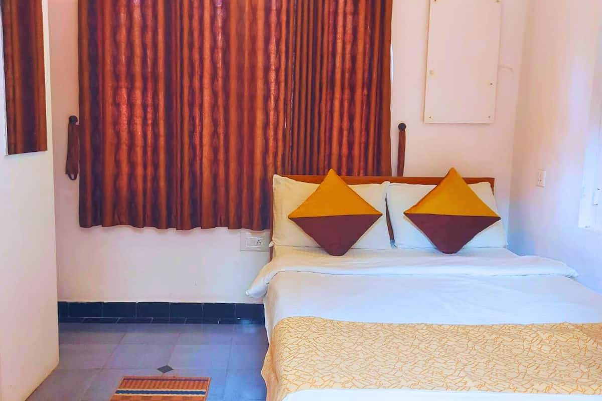 Une chambre d’hôtel avec un lit, deux oreillers ornés de motifs géométriques, une fenêtre avec des rideaux, un interrupteur fixé au mur et une porte.