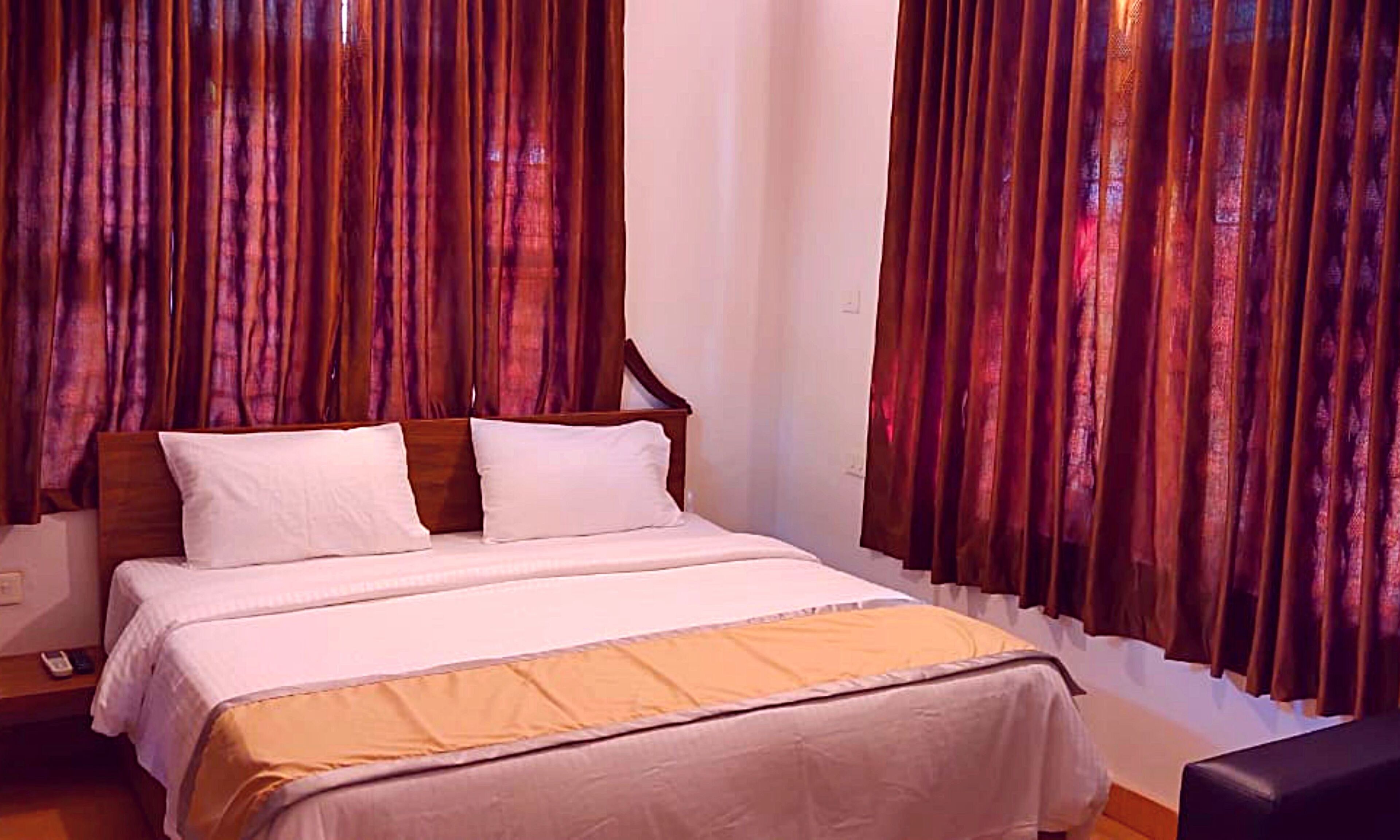 A bedroom with a wooden bed, white bedding, and curtains.