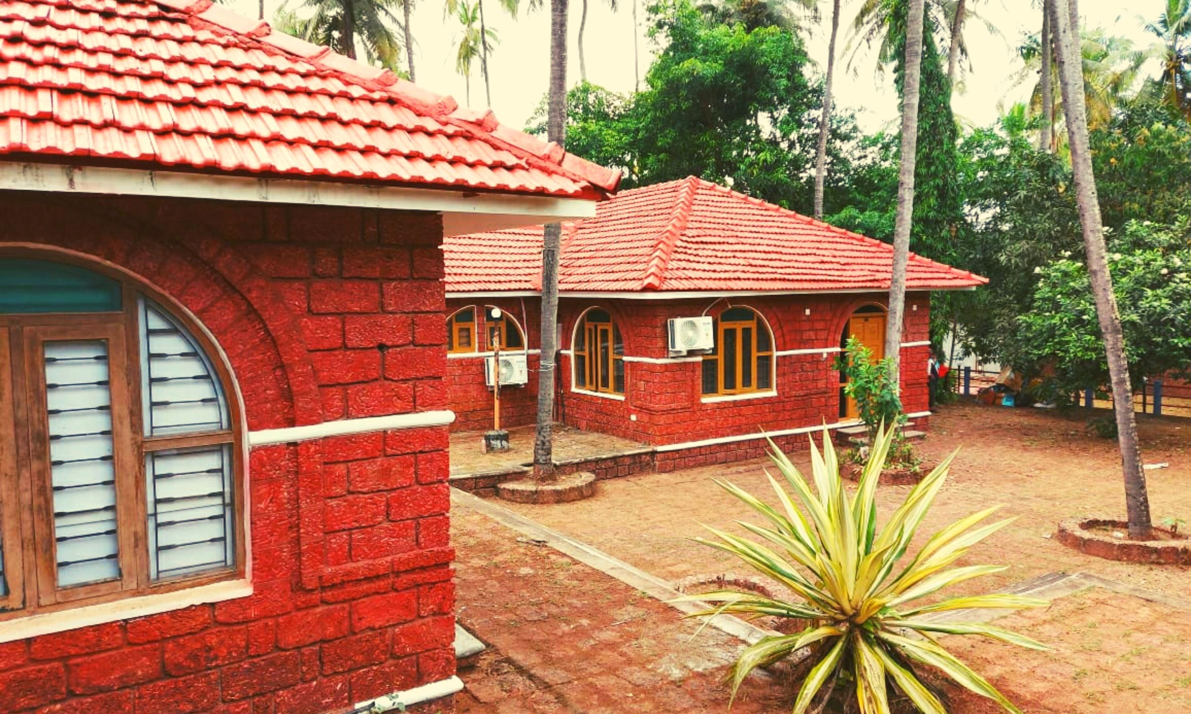 A red brick building with a tiled roof, arched windows, and a small garden area with a plant.