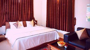 A hotel room with a large bed, a bedside table with a fruit basket, a black leather sofa, and dark curtains. - ShriGo Bekal Fort Resort & Spa (Hosdurg)