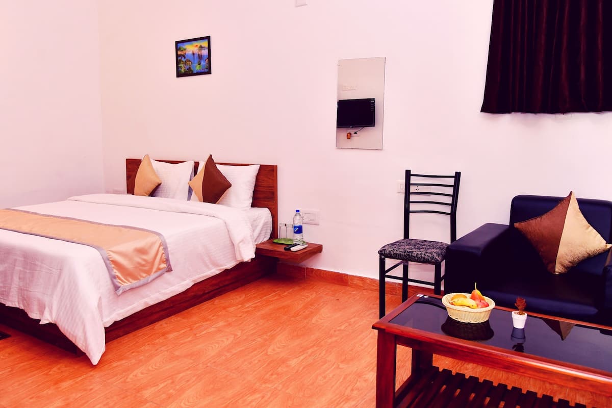 Une chambre d’hôtel comprenant un lit, une table de chevet, une chaise, une petite table et un téléviseur fixé au mur.