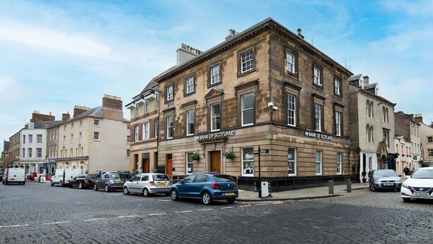En historisk bygning med et skilt, der viser 'Bank of Scotland', med klassisk arkitektur, mange vinduer og en murstensfacade.