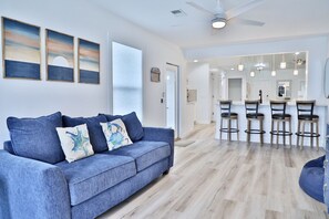 Un salon moderne avec un canapé bleu, un coin repas doté de tabourets de bar et un ventilateur de plafond.