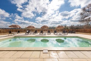 Piscina con sillas de descanso y sombrillas de paja, rodeada por una valla de madera.
