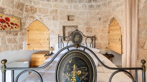 Habitación de paredes de piedra con una cama, armarios de madera y un cabecero decorativo de metal.