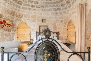 Una habitación con paredes de piedra, una cama, armarios de madera y un cabecero decorativo de metal.