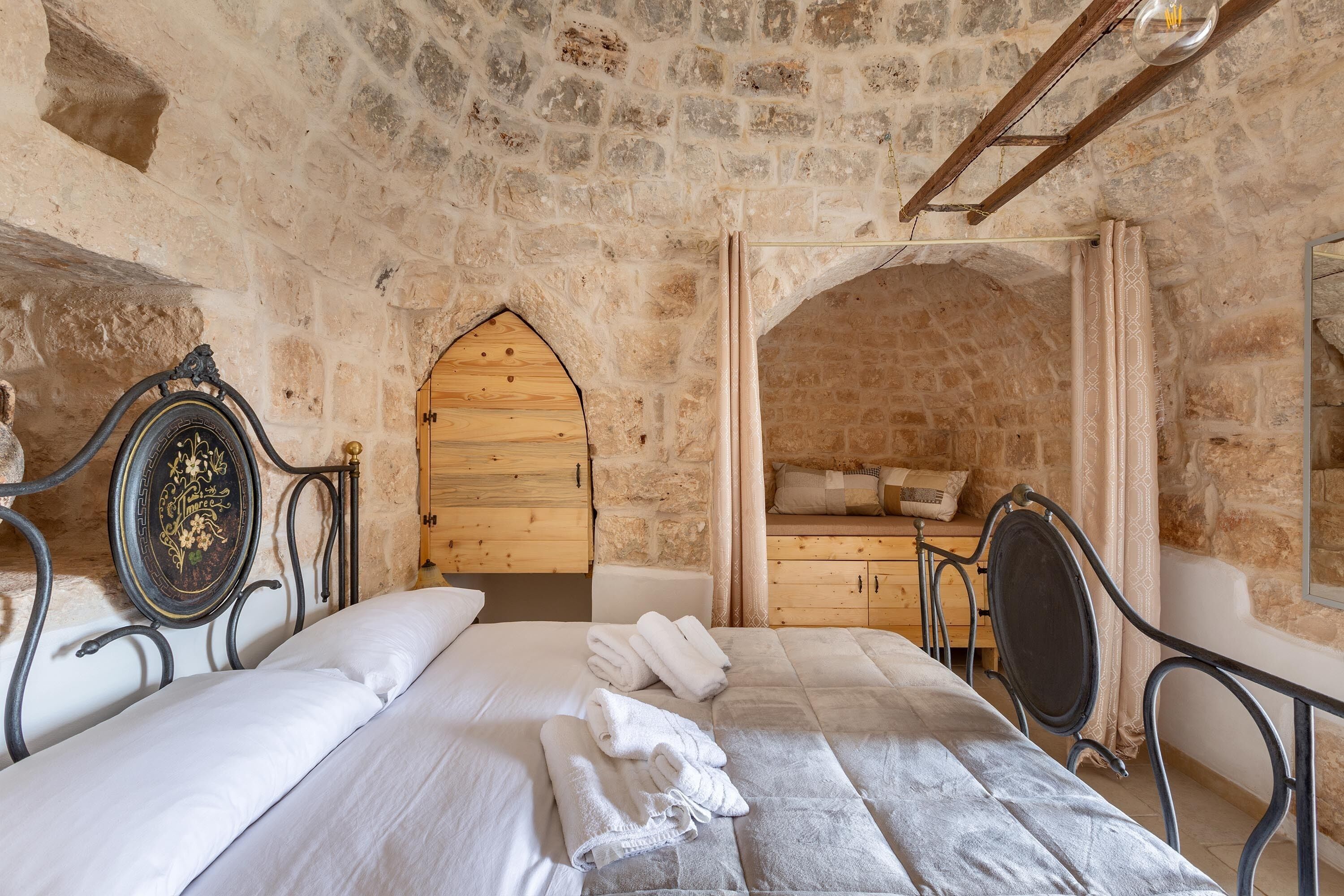 Un dormitorio con paredes de piedra, una cama, una puerta de madera y una pequeña zona de estar.