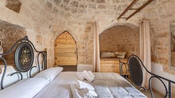 Un dormitorio con paredes de piedra, una cama, una puerta de madera y una pequeña zona de estar.